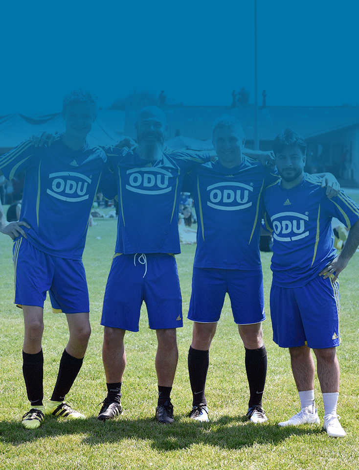 Four ODU employees wearing blue shirts stand together on a soccer pitch.